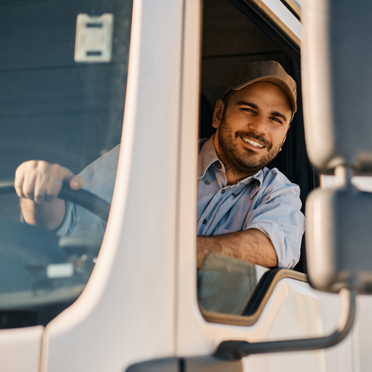 Happy professional truck driver driving his truck and looking at camera.